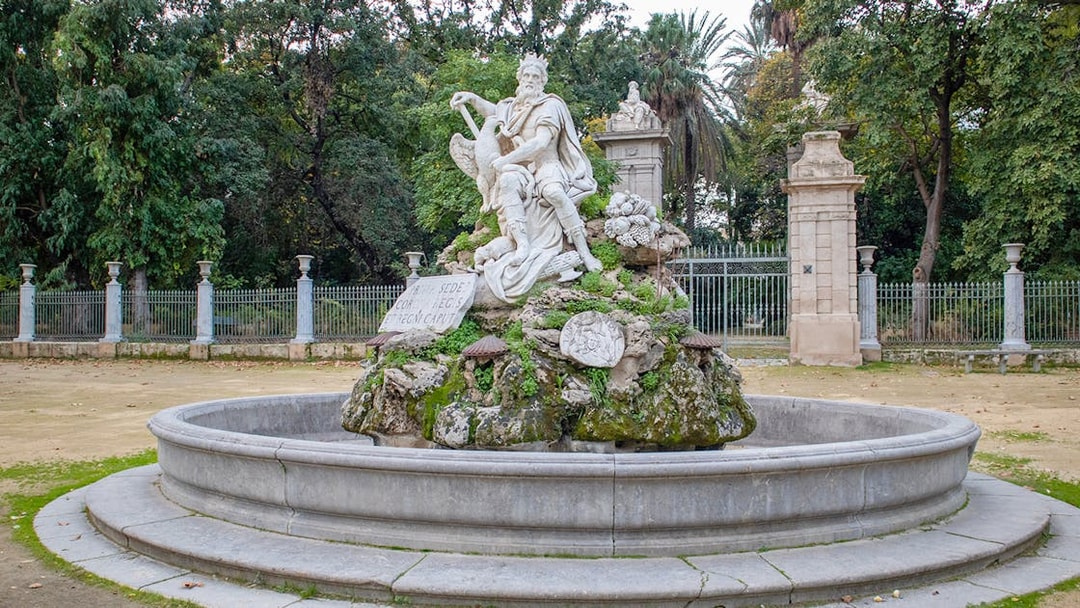 Statue in Orto Botanico garden, Palermo, surrounded by greenery and stone fence.