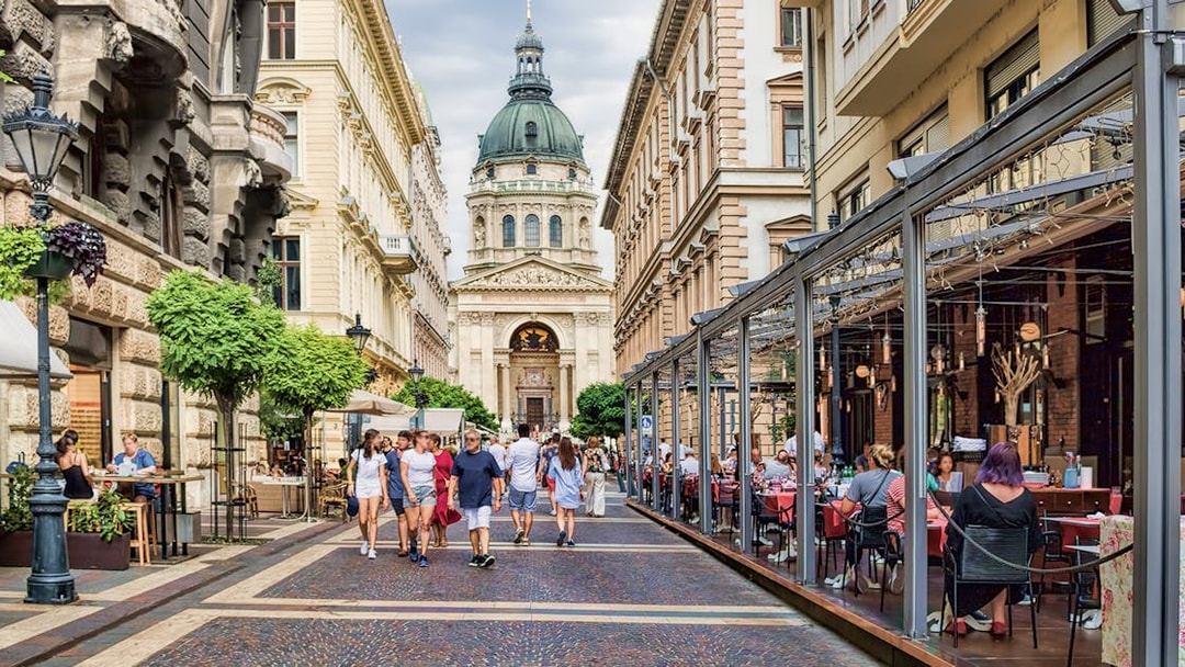 Street view of St. Stephen's Basilica in Budapest with people dining and walking.