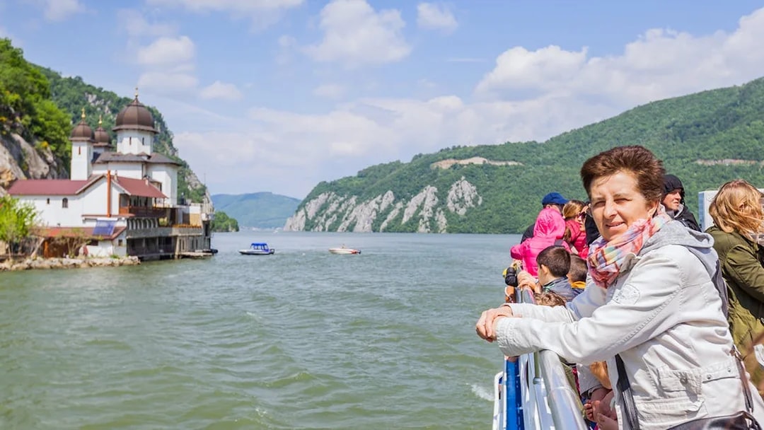 Tourists on a river cruise in Budapest, viewing a church and scenic hills.