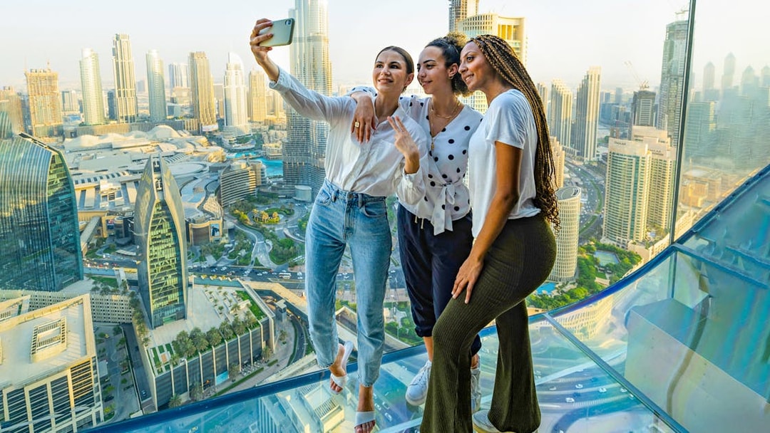 Three people taking a selfie on a glass observation deck overlooking a city skyline.