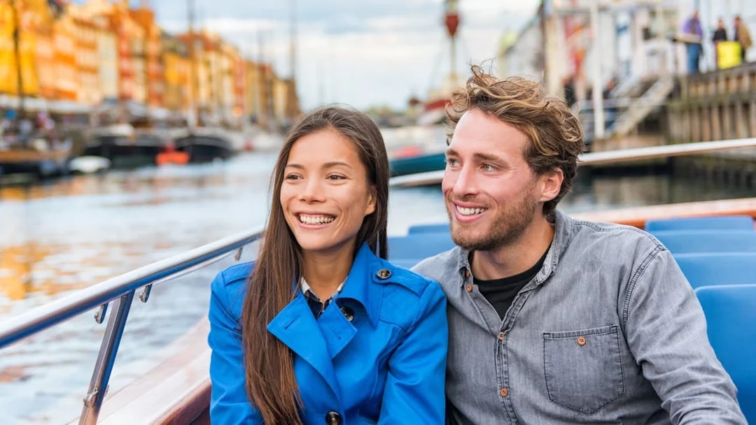 Tourist couple enjoying a boat tour on a canal with colorful buildings in the background.