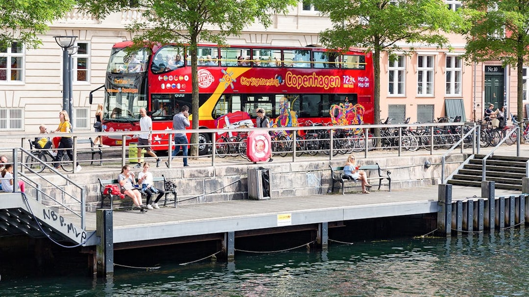 Hop-On-Hop-Off bus by canal in Copenhagen with people on the promenade.