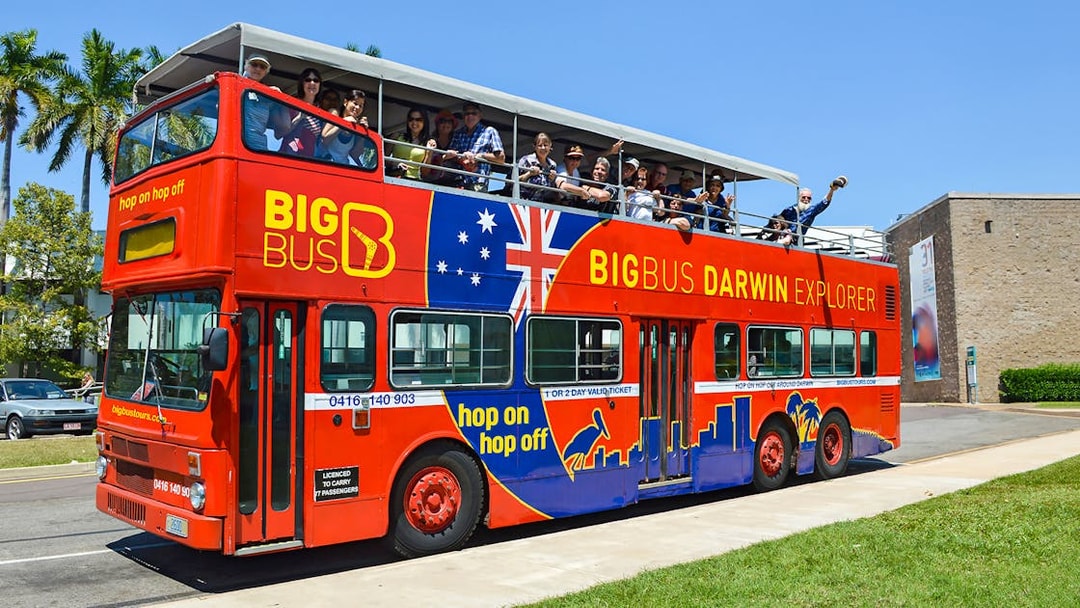 Open-top red bus with tourists on a Darwin city tour.