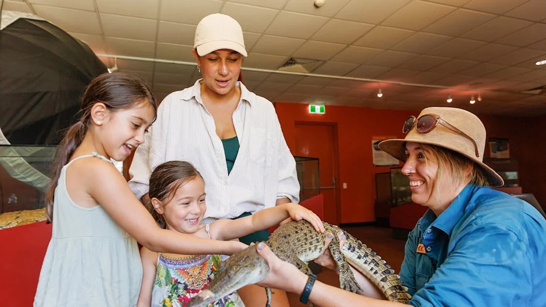 Two girls with a guide touching a young crocodile at Crocosaurus Cove, Darwin, Australia.