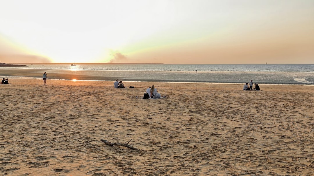 People enjoying sunset at Mindil Beach, Darwin, with sailboats on the horizon.
