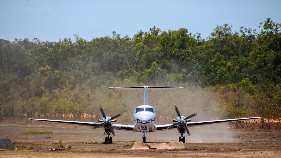 Small aircraft landing on a dirt runway surrounded by trees, part of Royal Flying Doctor Service tour.