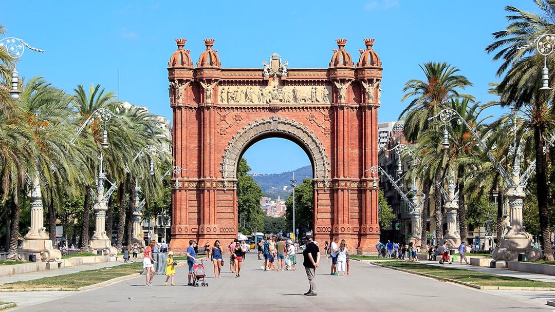 Arc de Triomf in Barcelona with people walking and palm trees lining the path.