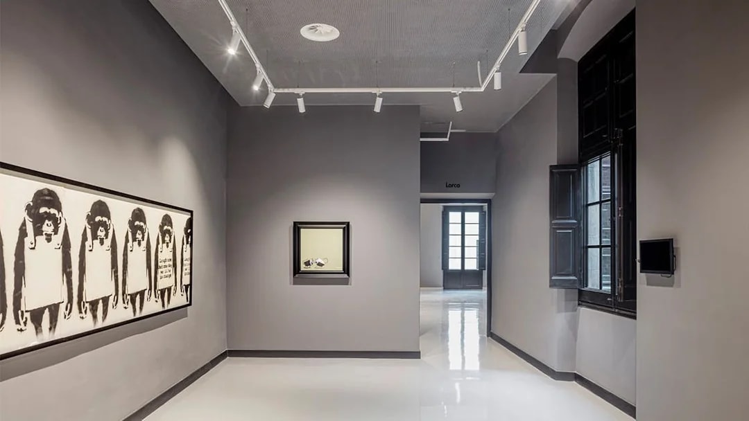 Exhibit of modern art at Moco Museum in Barcelona, featuring framed artworks on a gray wall.