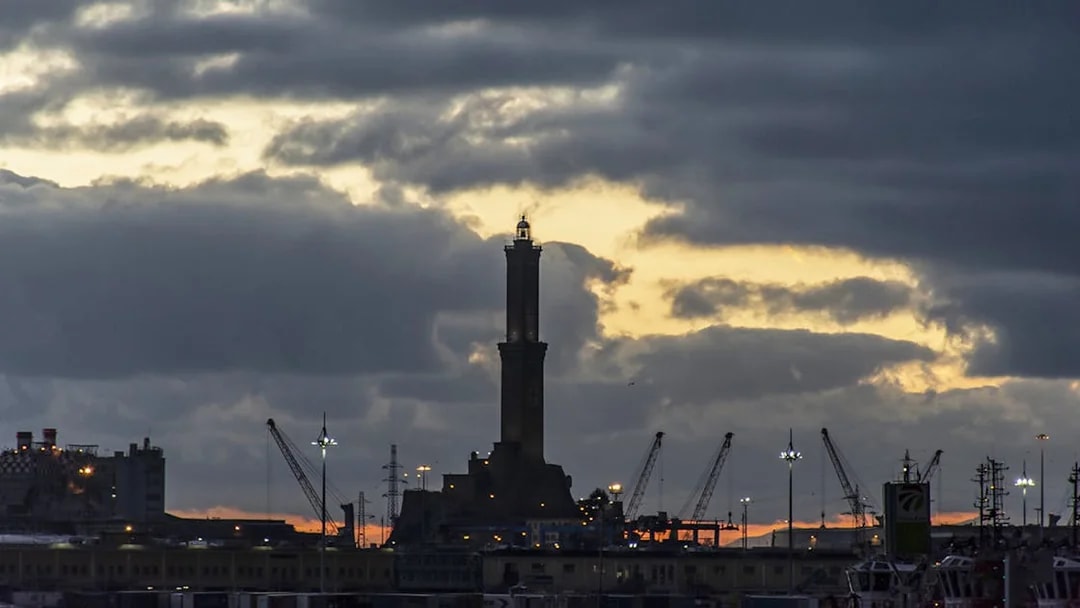 Genoa's Lighthouse at sunset with cranes in the harbor.