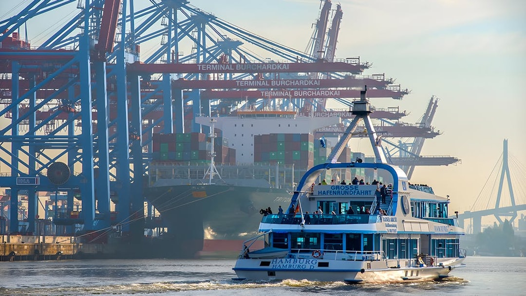 Hamburg harbor cruise ship passing container terminal cranes.