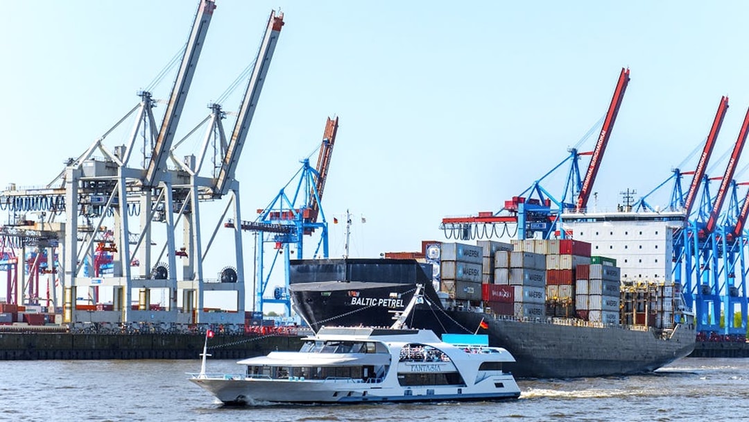 Harbor cruise boat passing container ship and cranes in Hamburg port.
