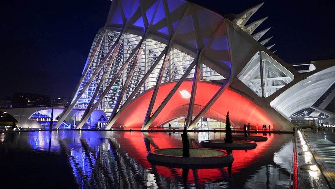 Hemisfèric and Science Museum Valencia illuminated at night, reflecting in water.