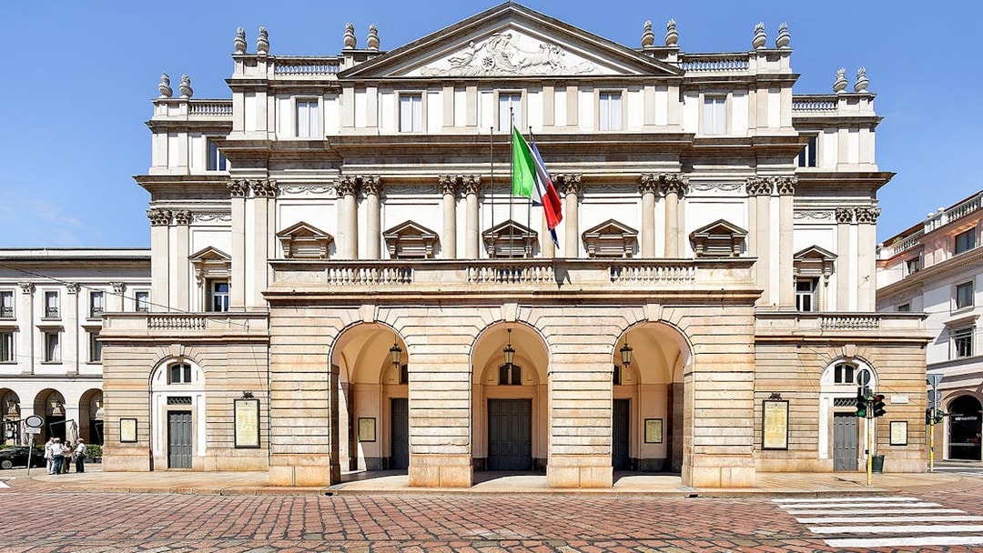 La Scala Theatre facade in Milan, Italy, with Italian flag displayed.