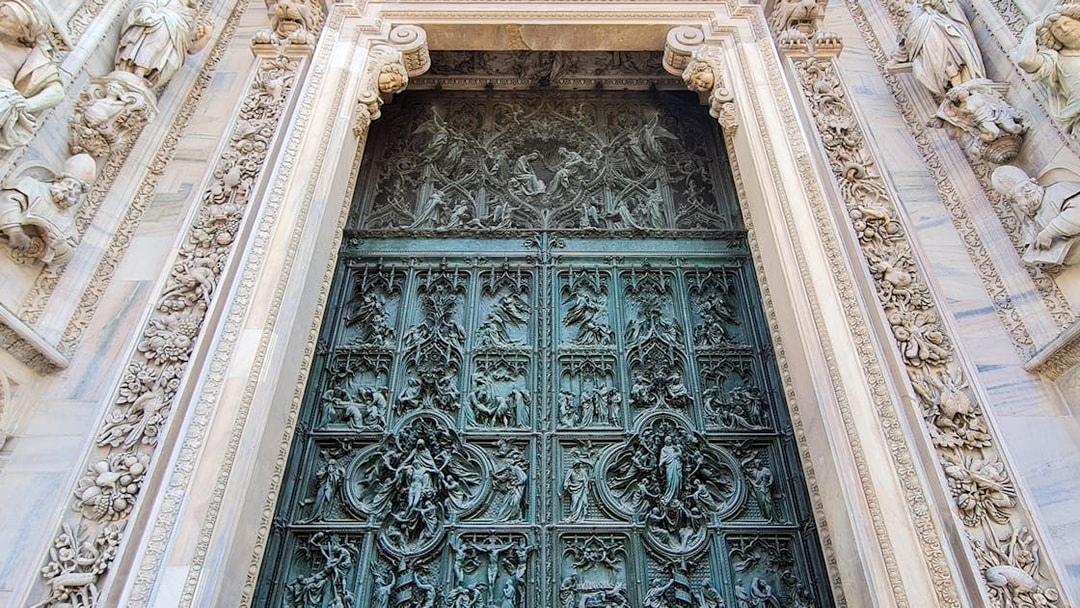 Ornate bronze door of Duomo Cathedral in Milan, featuring detailed religious carvings.