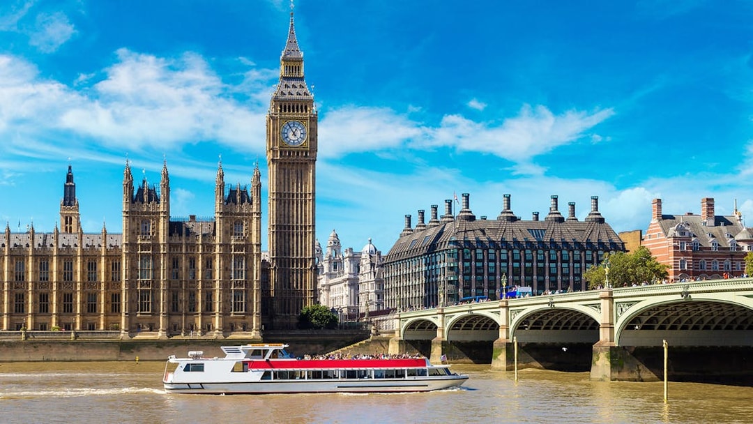 Thames River cruise boat passing Big Ben and Westminster Bridge in London.