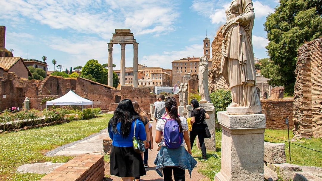 Visitors exploring the Roman Forum with ancient statues and ruins in Rome, Italy.