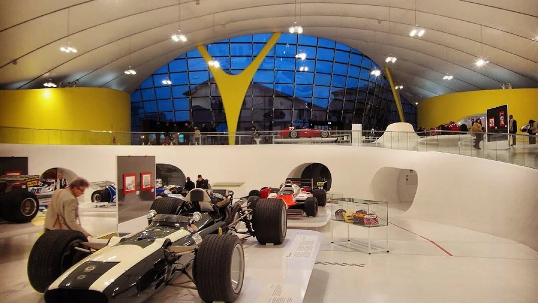 Ferrari race cars displayed at Modena Enzo Ferrari Museum with visitors exploring exhibits.