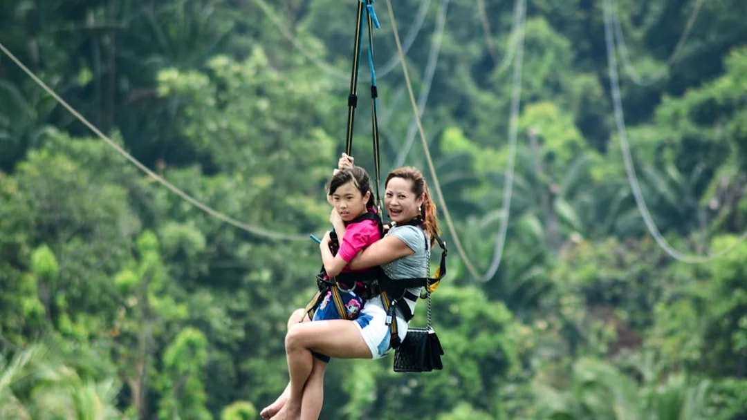 Two people zip-lining through lush greenery in Singapore.