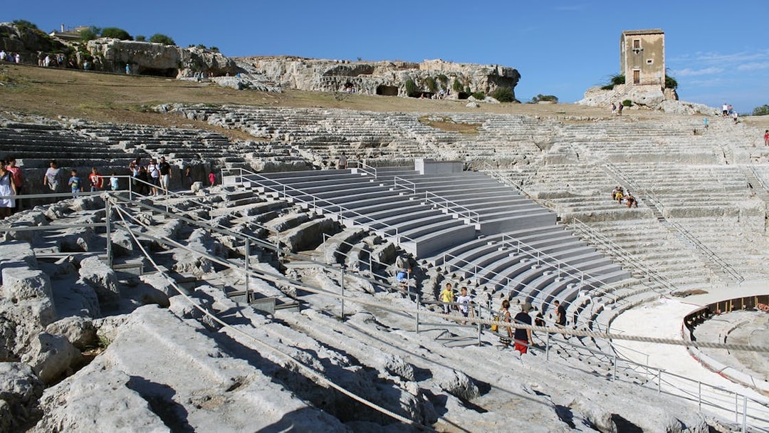 Greek Theater of Syracuse with visitors exploring ancient stone seating.