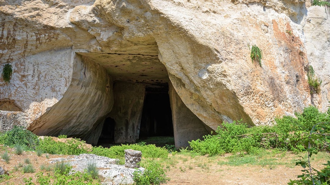Cave entrance at Neapolis Archaeological Park, Syracuse, surrounded by greenery.