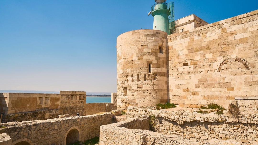 Maniace Castle stone walls and lighthouse overlooking the sea in Syracuse, Italy.