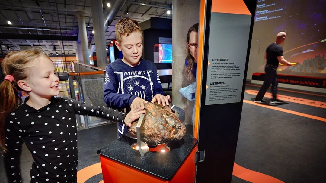 Children exploring a meteorite exhibit at NEMO Science Museum, Amsterdam.
