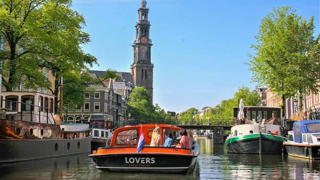 Canal cruise boat on Amsterdam canal with Westerkerk tower in the background.