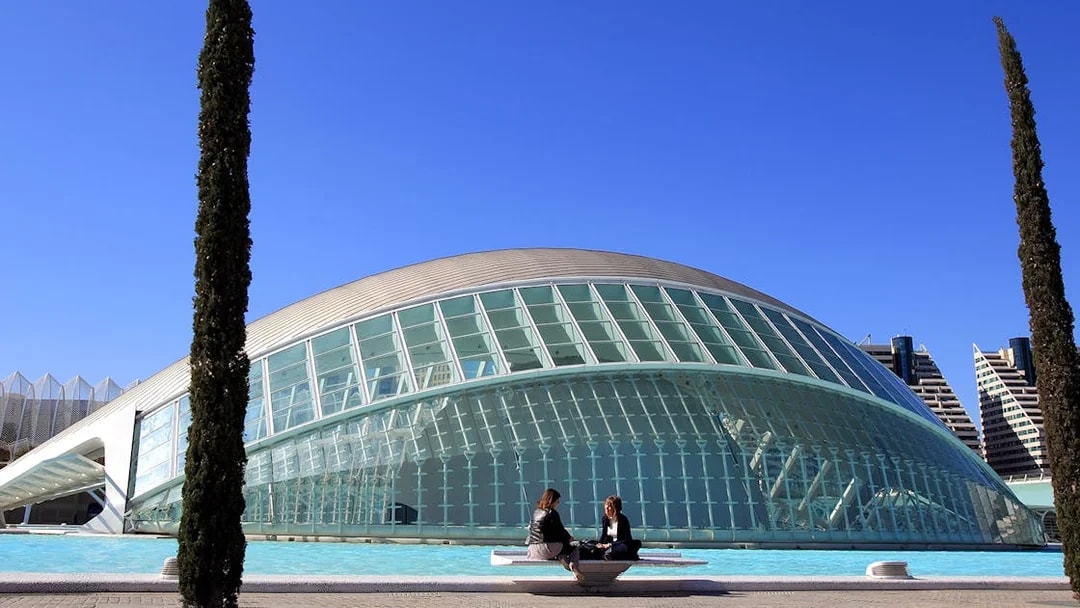 Hemisfèric building in Valencia with two people sitting by the reflecting pool.