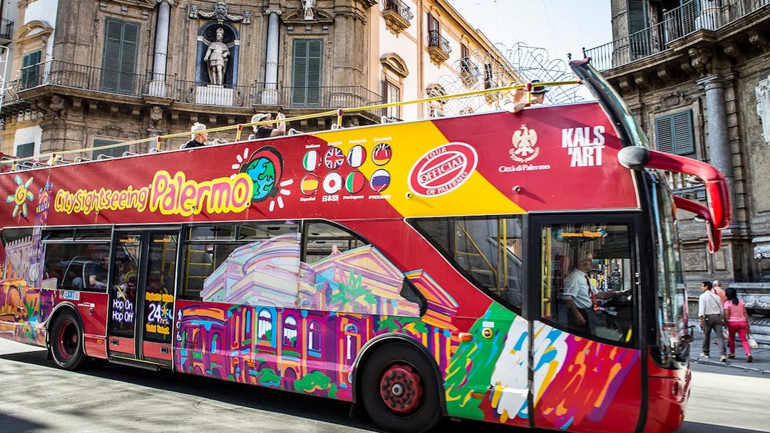 Palermo hop-on hop-off bus passing historic building in city center.