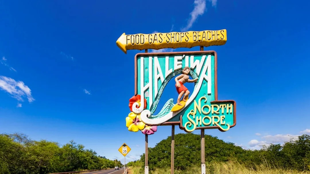 Haleiwa Town sign with surfer and North Shore text on a sunny day.