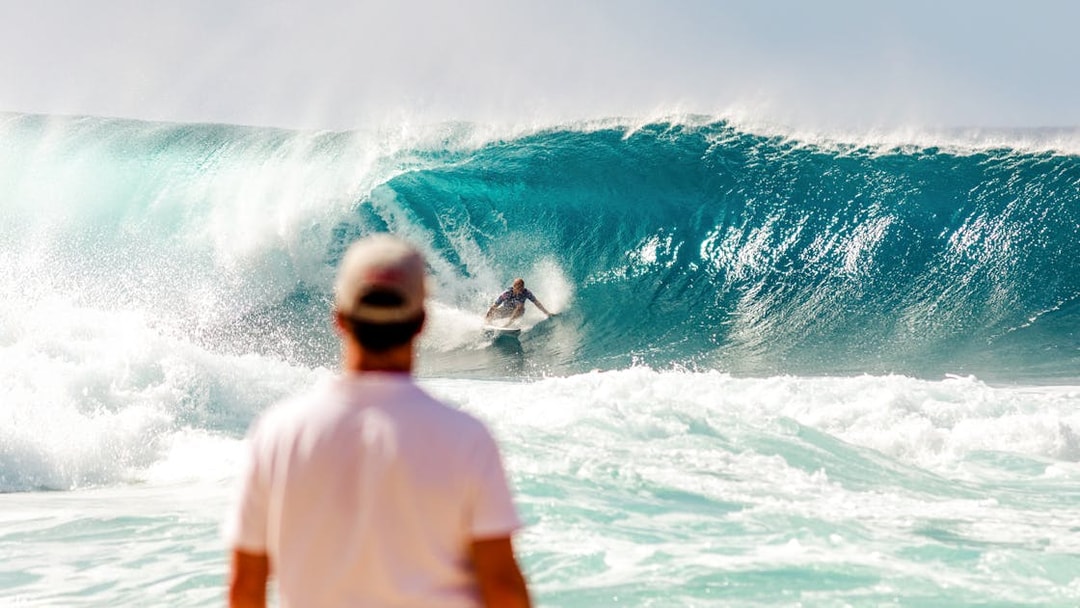 Tourist watching a surfer ride a large wave at the beach.