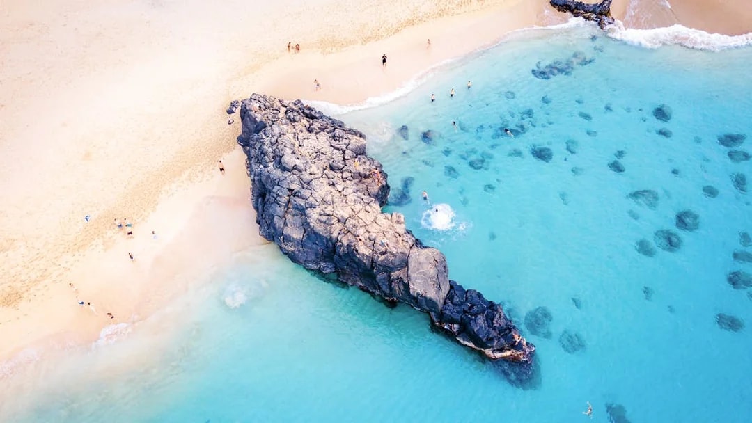 Waimea Beach rock formation with swimmers in clear blue water, Oahu, Hawaii.