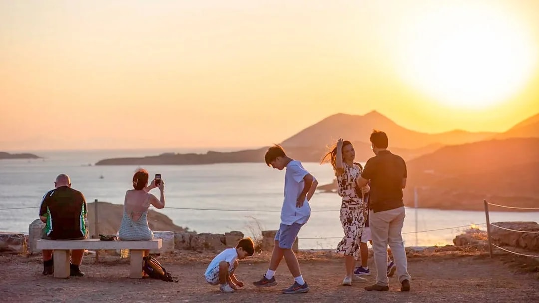 Guests watching sunset at Cape Sounion with sea and mountains in background.