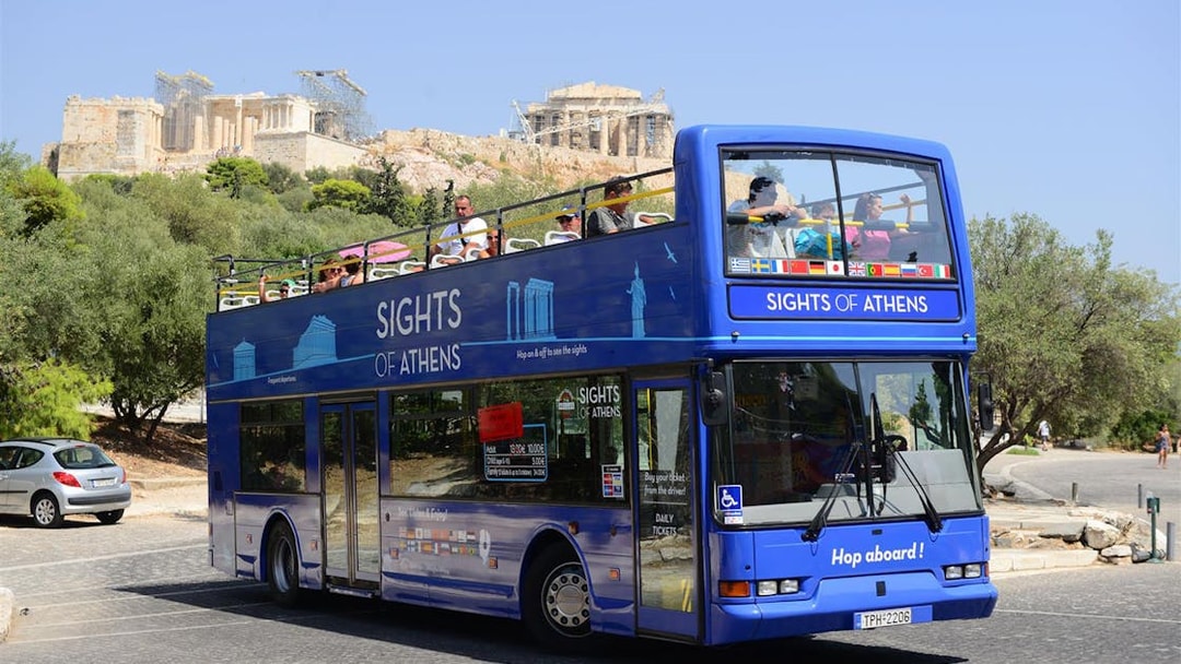 Open-top tour bus in Athens with Acropolis in the background.