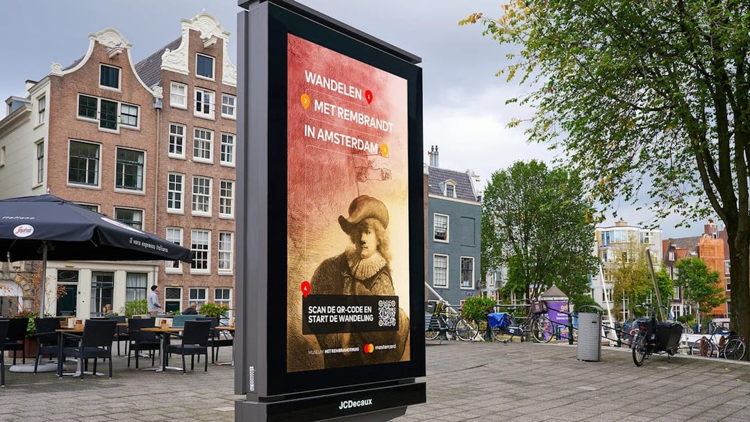 Outdoor sign promoting Rembrandt House tour in Amsterdam city square.