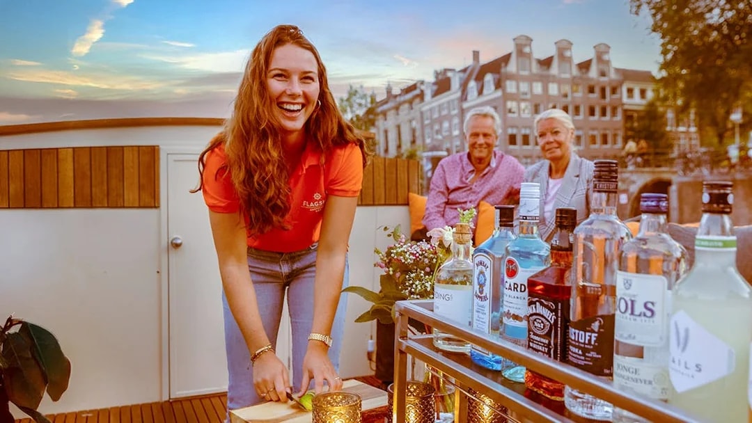 Bar on Amsterdam canal boat with drinks and bartender preparing lime slices.