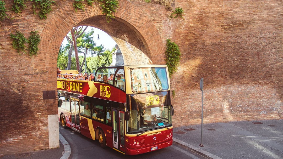 Open-top Big Bus tour passing through ancient Roman arch in Rome.