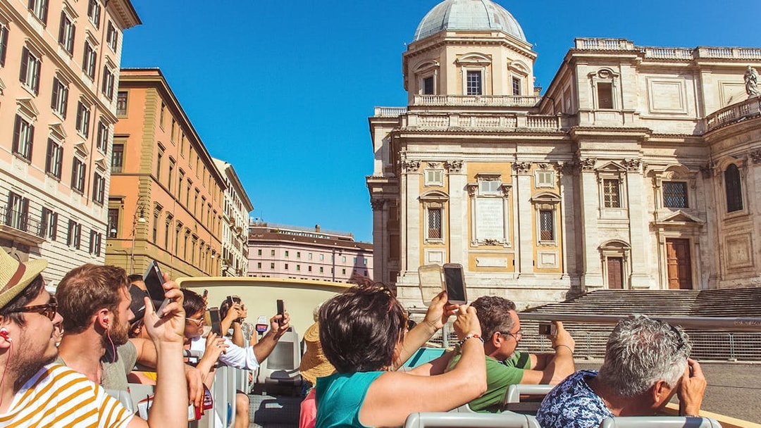 Tourists on a hop-on hop-off bus tour in Rome, photographing a historic building.