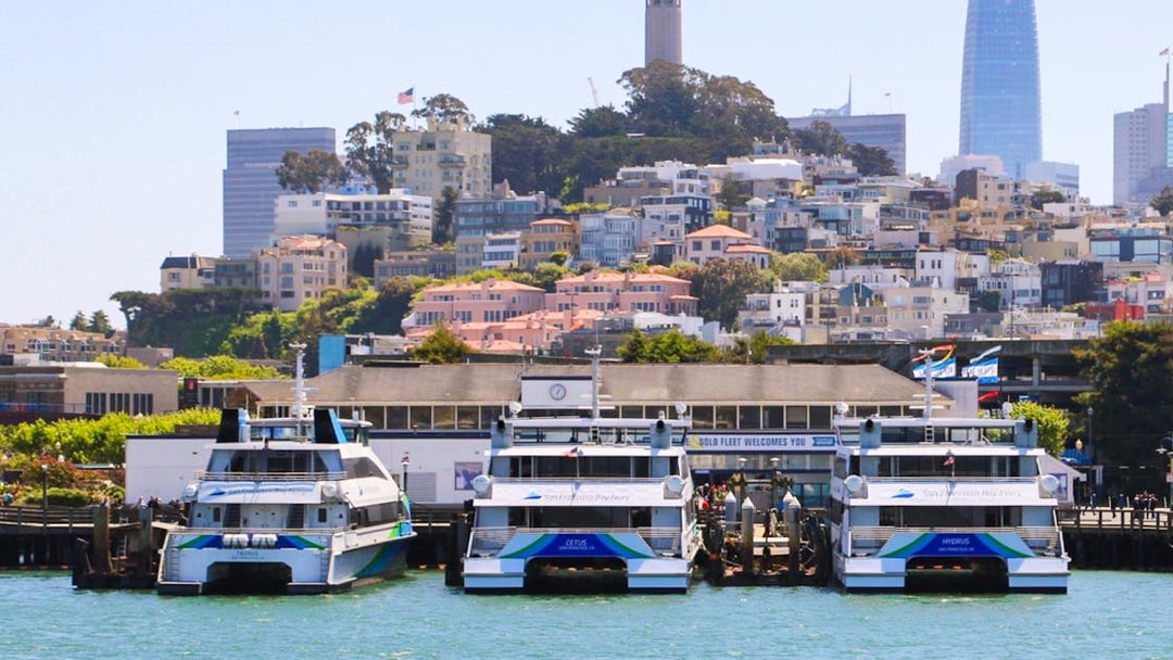 Boats docked at San Francisco Bay with cityscape and Coit Tower in the background.