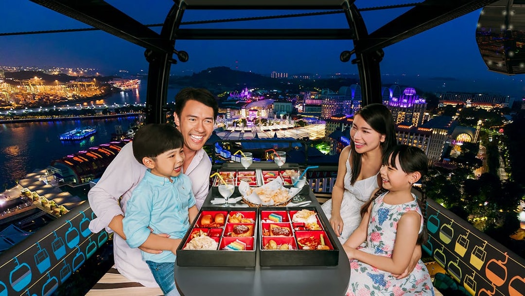 Family dining in Singapore Cable Car with city lights view.