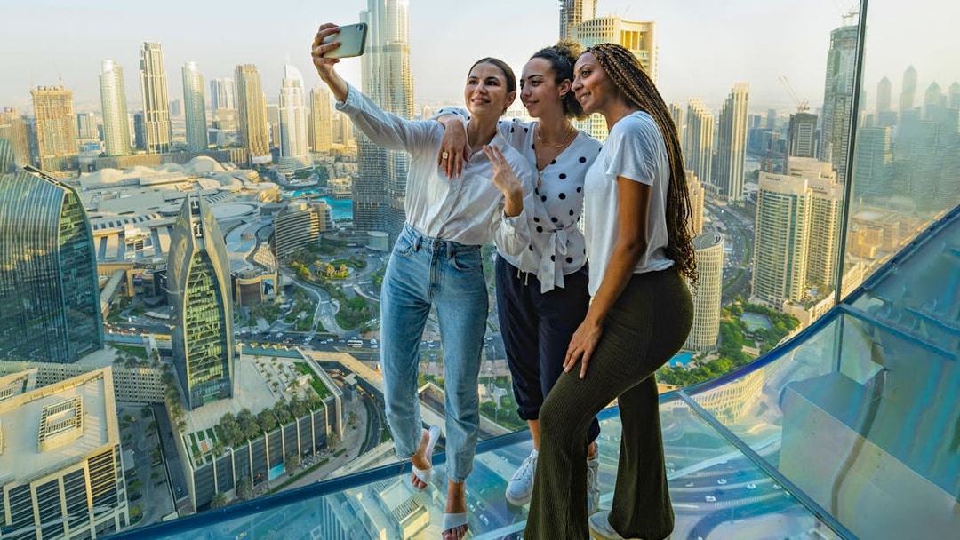 Visitors taking a selfie on the glass floor of Sky Views Observatory, Dubai skyline in background.