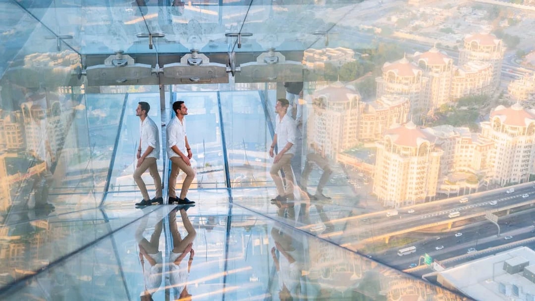 Man walking on glass slide at Sky Views Observatory with cityscape below.