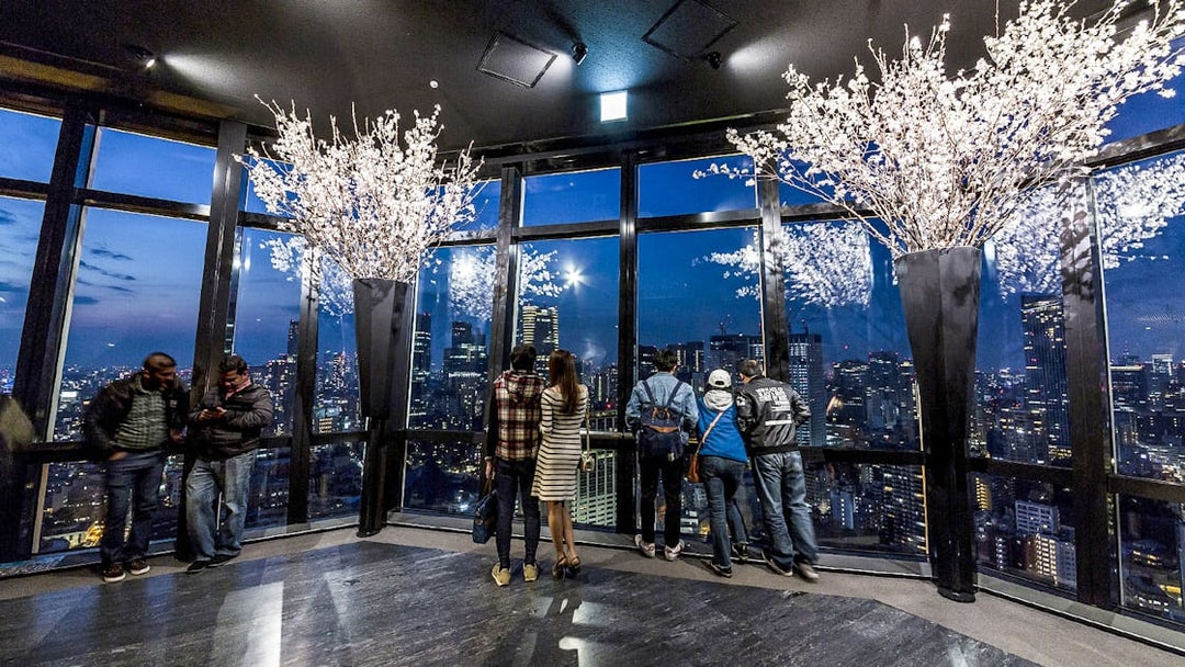 Tokyo Tower observation deck with visitors overlooking city skyline at night.