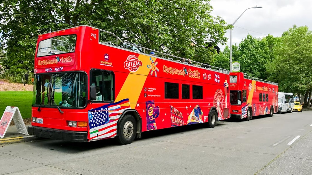 Red double-decker tour bus in Seattle with sightseeing graphics parked by trees.