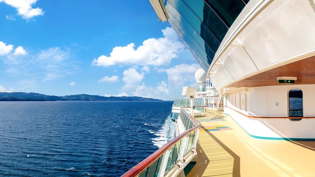 Cruise ship deck overlooking ocean and distant coastline on a sunny day.