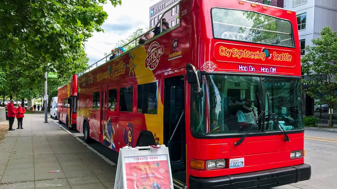 Red double-decker tour bus parked in Seattle street with ticket sign nearby.
