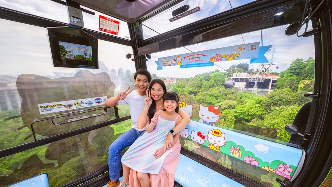 Family enjoying a ride in the Hello Kitty-themed Singapore Cable Car with lush greenery outside.
