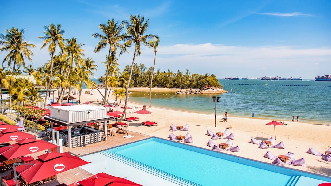 Sentosa beach view with palm trees, pool, and dining area, Singapore.