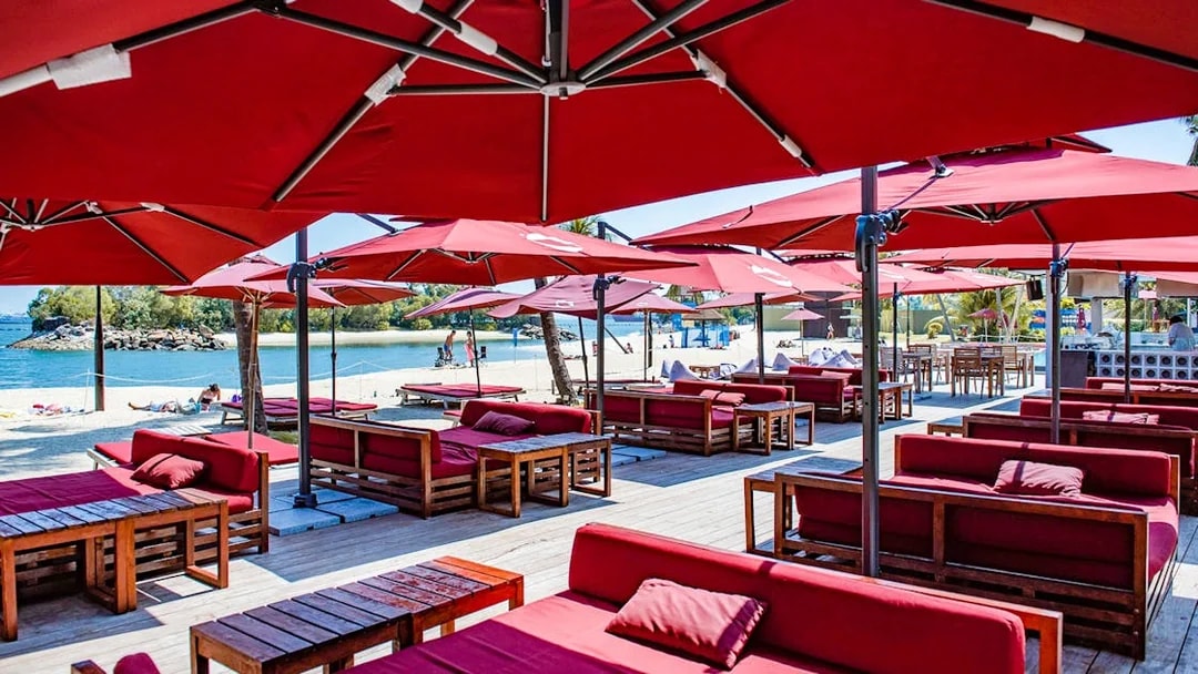 Outdoor dining area with red umbrellas and seating at Sentosa Beach, Singapore.