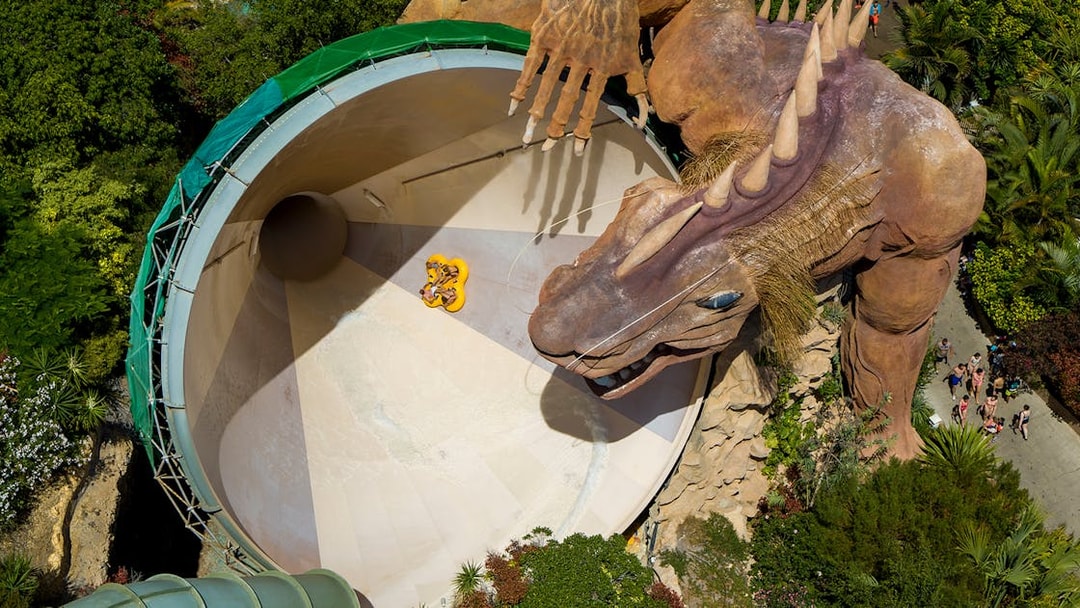 Riders on Cyclone slide with dragon at Siam Park, surrounded by lush greenery.